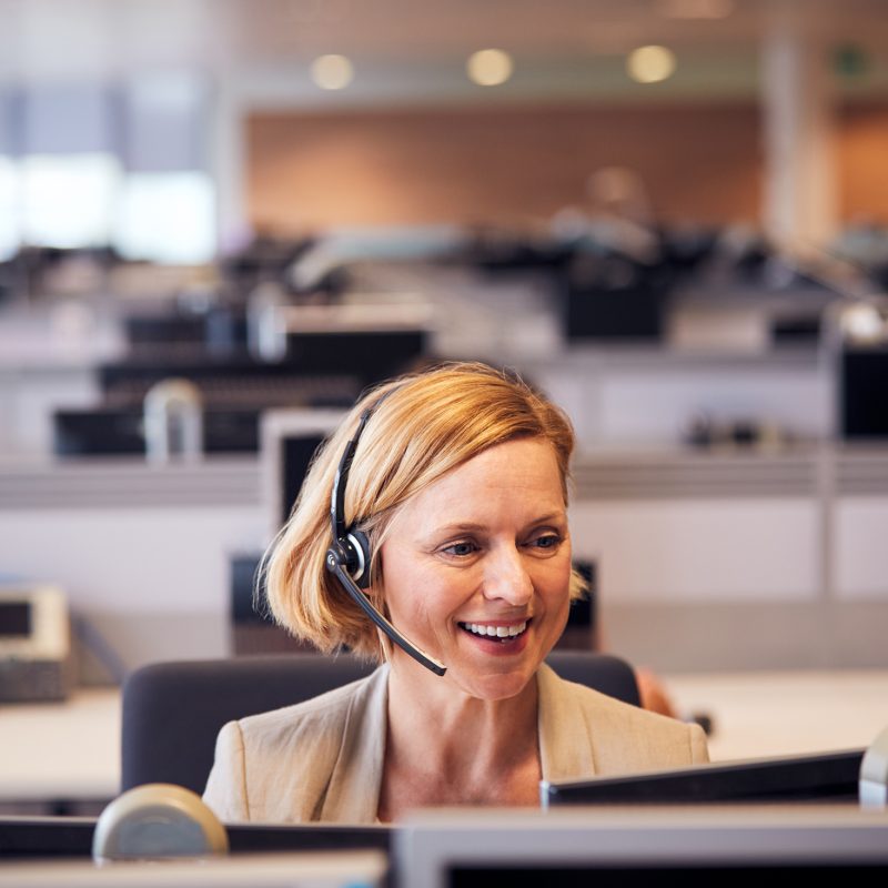 Mature Businesswoman Wearing Telephone Headset Talking To Caller In Customer Services Department
